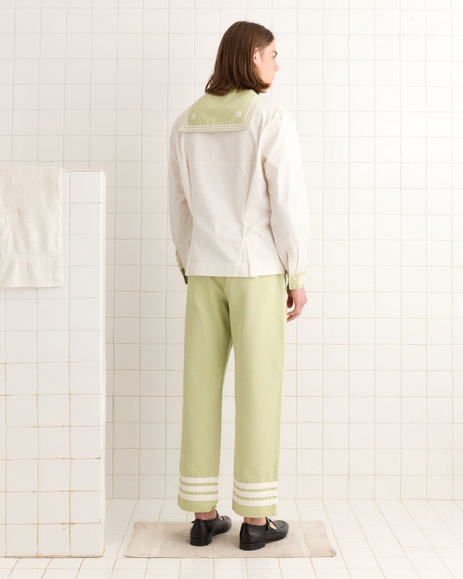 A person wearing the 1935 Cricket Shirt with light green and white colors and a sailor collar is standing in a tiled room, facing away.
