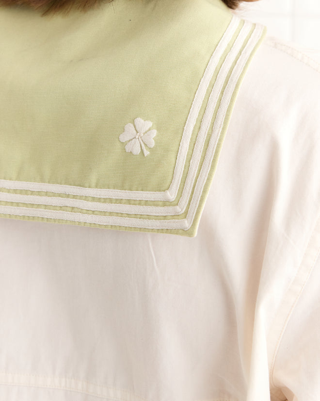 The 1935 Cricket Shirt is an antique-style white shirt featuring a light green sailor collar, crafted from natural-toned cotton and embellished with an embroidered four-leaf clover.
