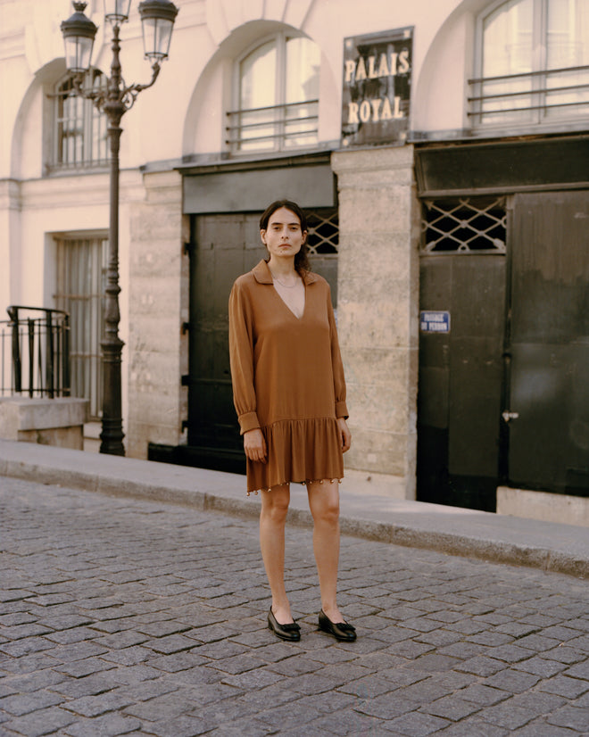 A woman wearing the Eddy Dress stands on a cobblestone street in front of the Palais Royal building.