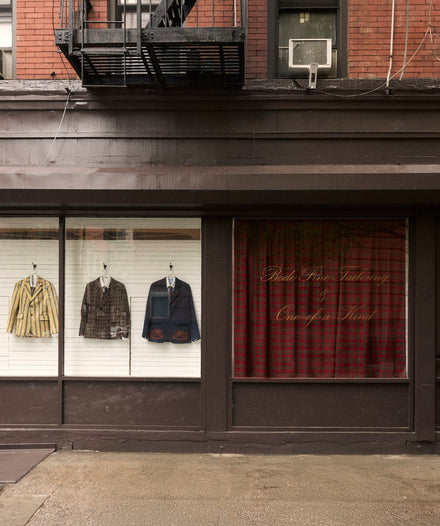 Storefront with clothing displayed in a window and red plaid curtain inside.