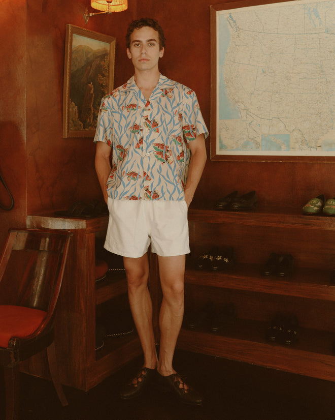 A person wearing the Swimmers Short Sleeve Shirt and white shorts stands indoors by shoe shelves and a U.S. map, highlighting this classic midcentury style.