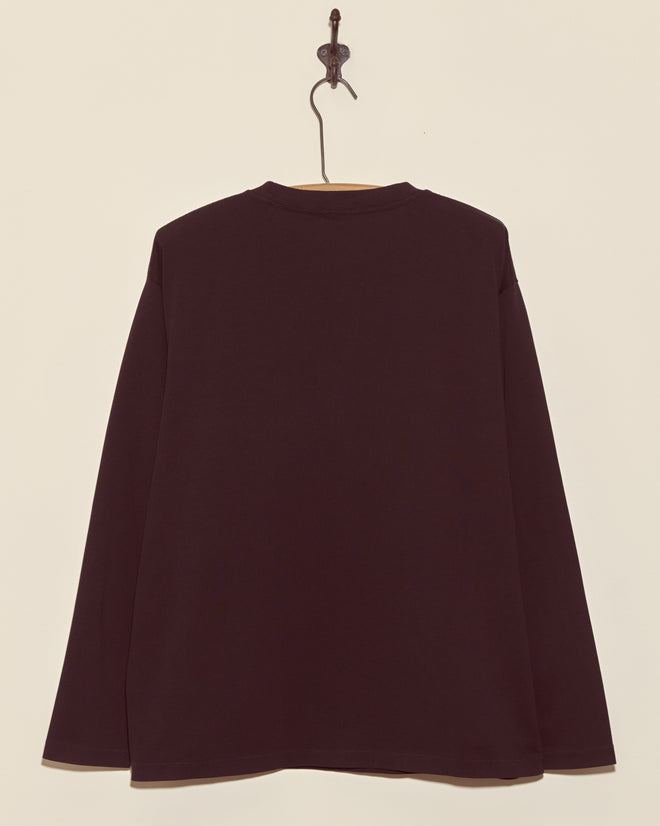 The Skeleton Long Sleeve Tee, featuring a boxy fit in plain black, hangs on a wall hook and is displayed from the back.