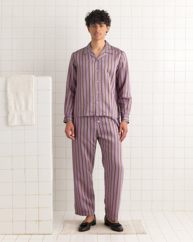 A person wearing the Alumni Stripe Long Sleeve Shirt - Purple, inspired by vintage 1960s-1980s style, stands in a white tiled room beside a towel hanging on the wall.