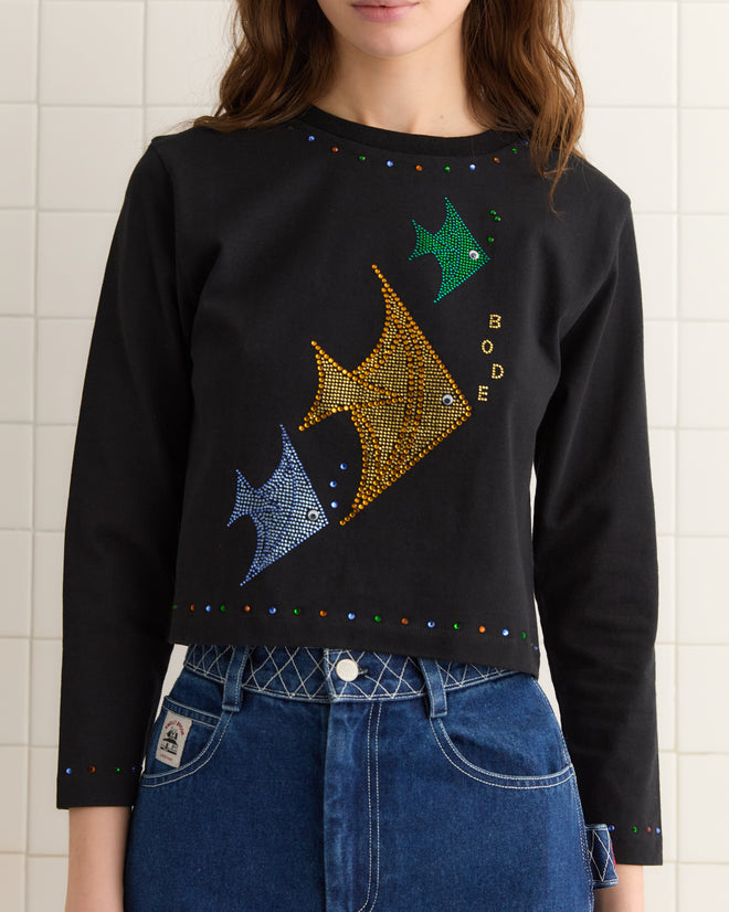 A person wearing the Angel Fish Tee - Black, made from 100% cotton, adorned with vibrant angelfish designs and discreet rhinestones for sparkle, paired with blue jeans.