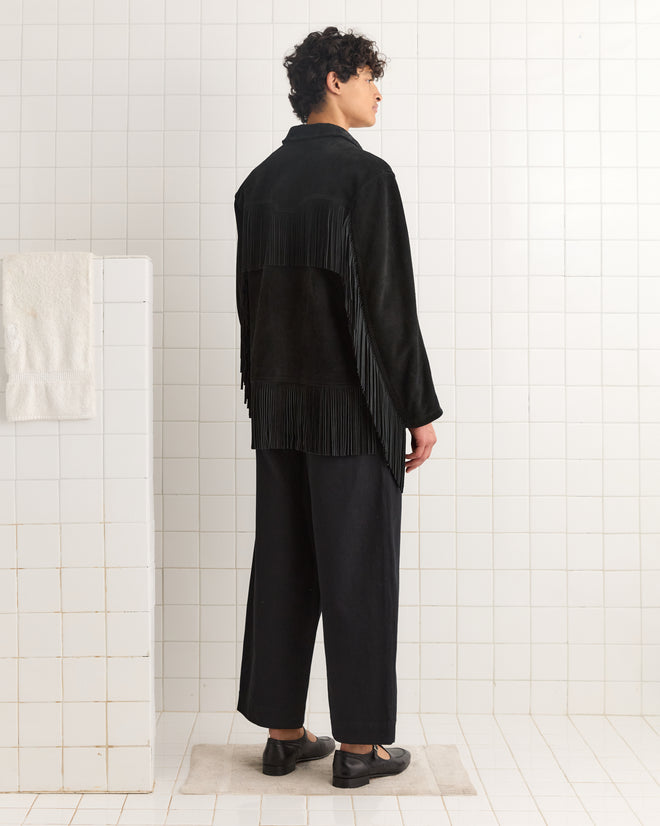 A person wearing the Appalachian Jacket - Black and wide-leg pants stands on a mat in a white tiled room, facing away.