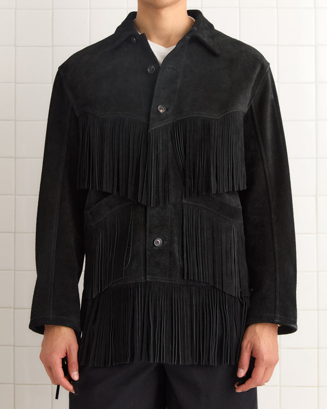 A person wearing the Appalachian Jacket - Black, a suede Western style with long fringe detailing, stands against a tiled wall.