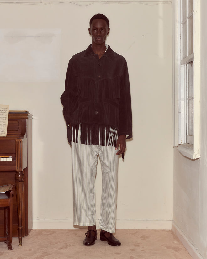 A man stands indoors by a piano and window, wearing the Appalachian Jacket - Black with striped pants, evoking a touch of Western flair.