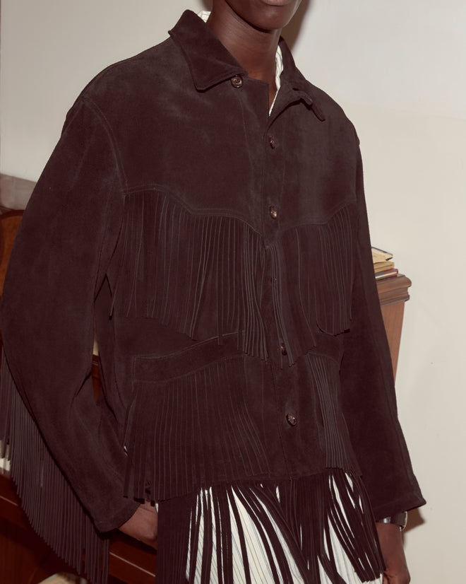 A person wearing the Appalachian Jacket - Black, a Western-style suede jacket with hand-cut fringe, stands indoors against a neutral background.