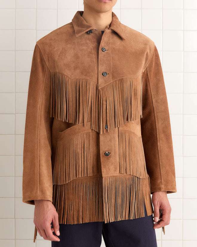 Person wearing the Appalachian Jacket - Light Brown, featuring hand-cut fringe details on the chest and waist, standing against a tiled wall.