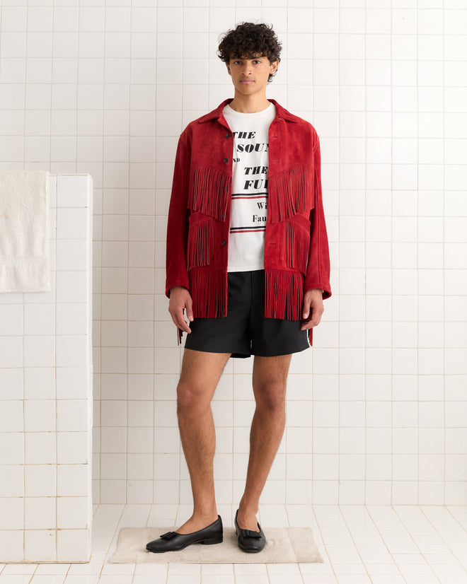 A person in an Appalachian Jacket - Red, white graphic tee, black shorts, and black loafers stands in a tiled room.