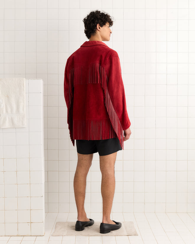 A person wearing the Appalachian Jacket - Red with hand-cut fringe, black shorts, and black shoes stands in a tiled room facing away.