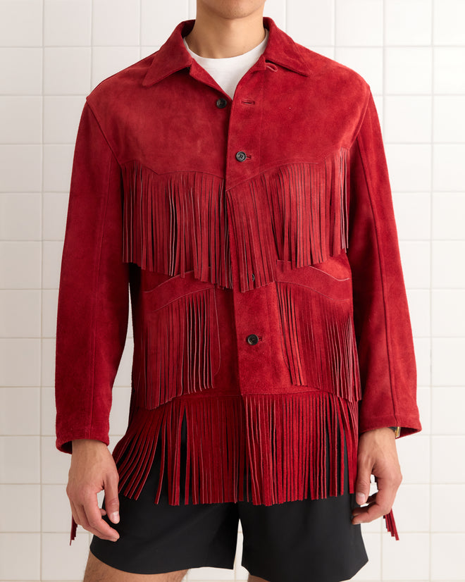 A man wears the Appalachian Jacket - Red, featuring hand-cut fringe details, over a white shirt and black shorts.