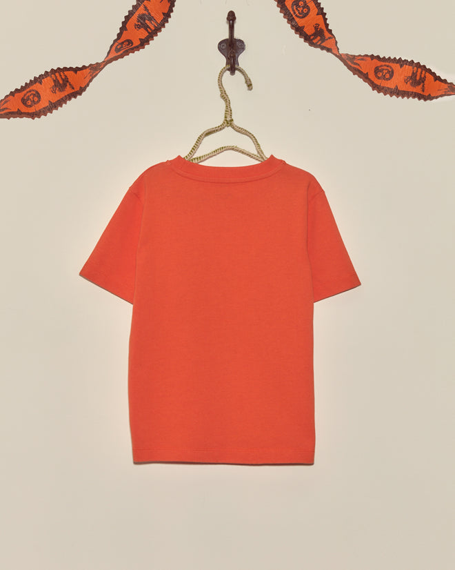 A Pumpkin Kids' Tee hangs on a hook below a Halloween-themed garland on a plain wall.