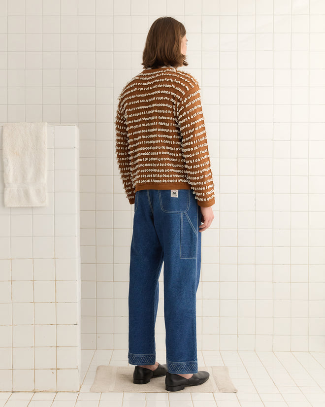 A person with shoulder-length hair is wearing a Beaded Cardigan paired with blue jeans, standing in a tiled room.