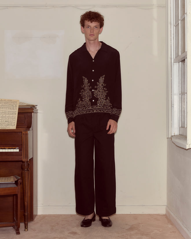 A person stands indoors in a Beaded Epoque Long Sleeve Shirt beside a piano near a window on a beige carpet.