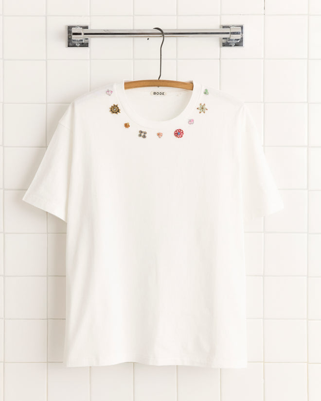 Beaded Floral Necklace Tee—white tee made from 100% cotton, featuring small, colorful vintage sari appliqués embroidered around the collar, shown on a wooden hanger.