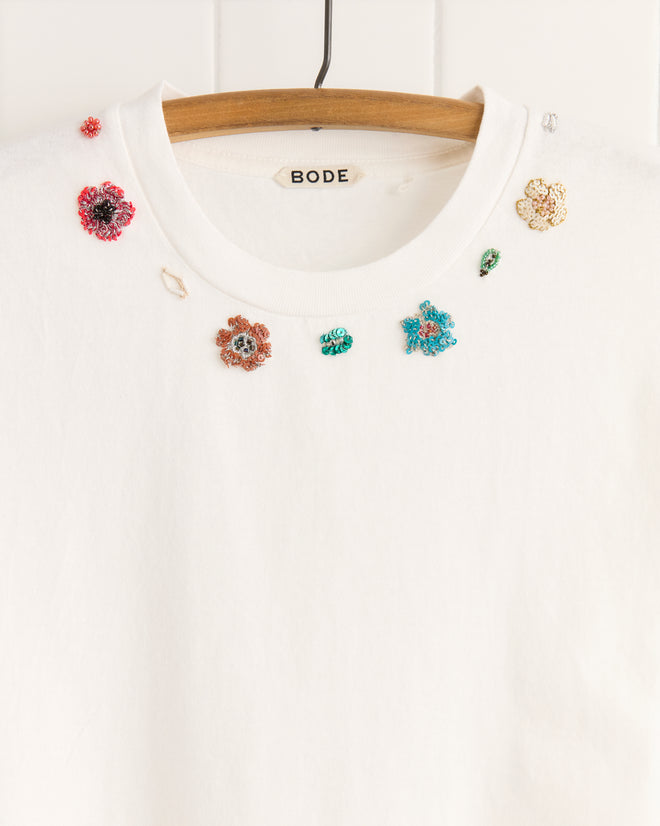 Beaded Floral Necklace Tee: 100% cotton white T-shirt with colorful beaded floral embroidery near the neckline, displayed on a wooden hanger.