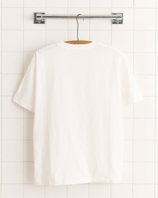 Beaded Floral Necklace Tee made from 100% cotton, displayed on a wooden hanger against a white tiled wall.