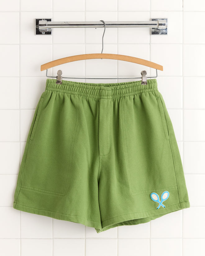 Beaded Racquet Patch Shorts in green, featuring front pockets and a small blue beaded tennis racquet patch, displayed on a wooden hanger.