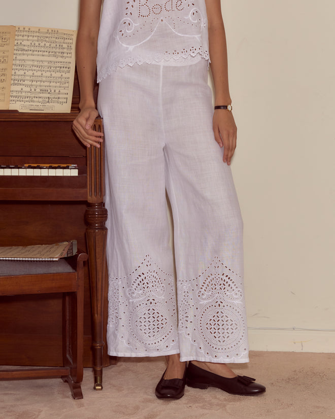 A person in Belvoir Pants and black flats stands beside a piano with sheet music on top.
