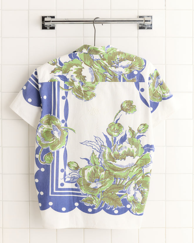 Blueberry Polka Dot Shirt - S/M: Short-sleeve vintage shirt with a unique green and blue geometric floral pattern, displayed on a metal rack in front of a white tiled wall.