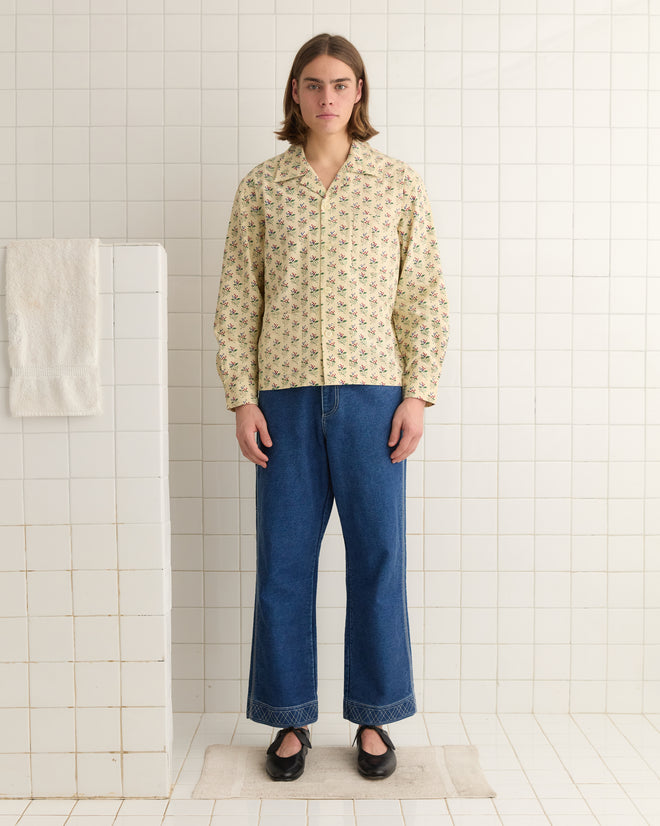 In a tiled room, someone wears the Boston Flower Long Sleeve Shirt paired with jeans, and a towel hangs nearby.