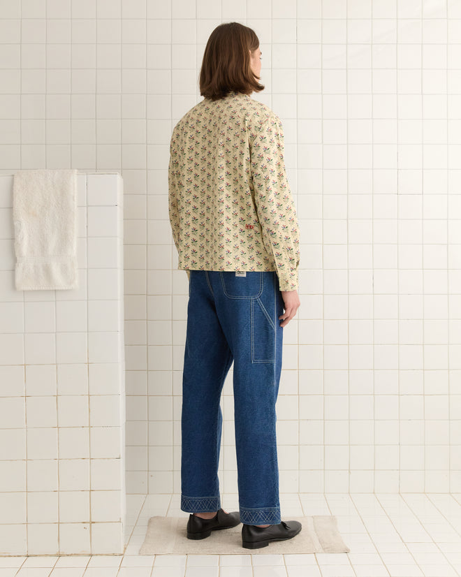 A person with long hair, wearing the Boston Flower Long Sleeve Shirt and jeans, stands on a white tiled floor facing away.
