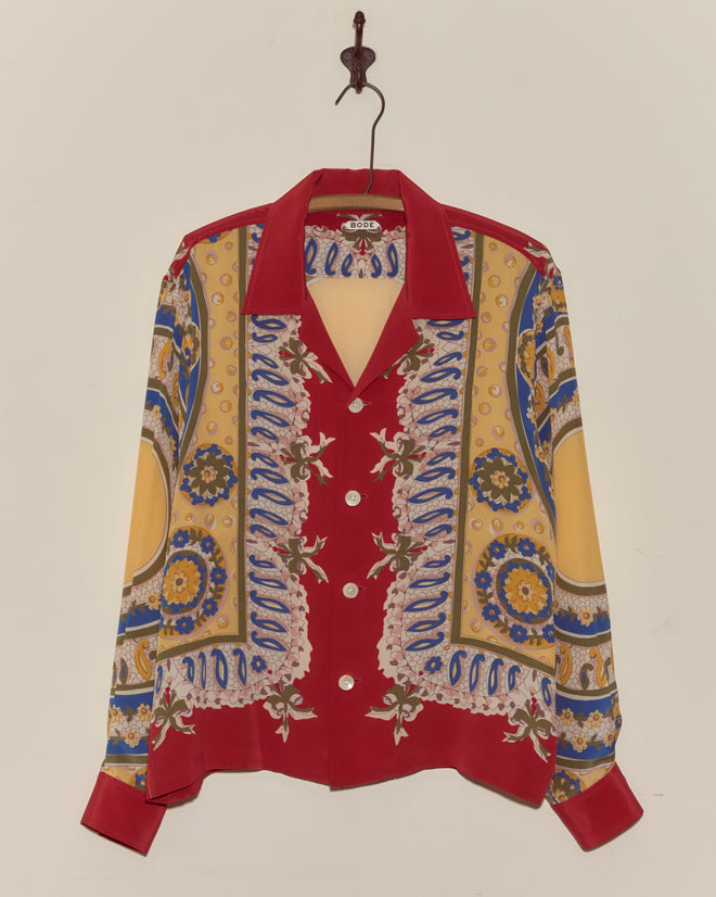 The Bricolage Long Sleeve Shirt is a vibrant 1960s-inspired button-up with red, yellow, and blue patterns, hanging on a hook.