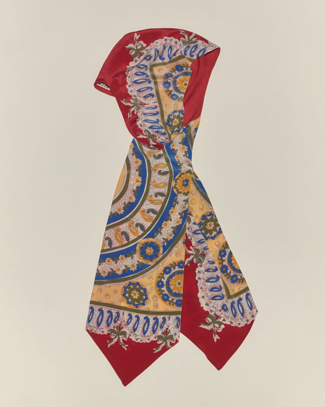 The Bricolage Driving Cap is perfectly accented by a silk scarf featuring red edges and gold, blue, and white patterns—an ideal touch for a vintage-inspired look.