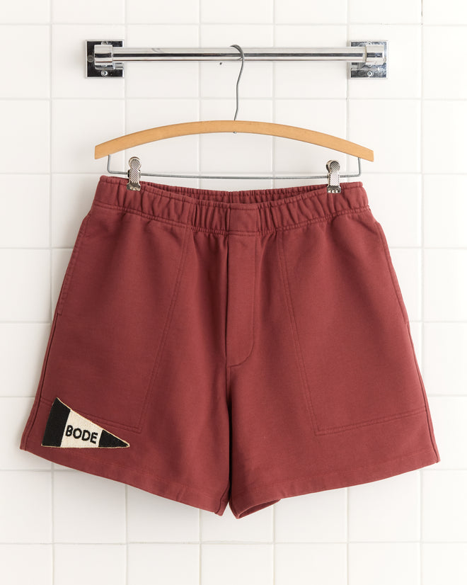 Burgundy Pennant Shorts hanging on a hanger, featuring a