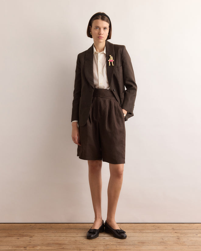 A person wears a brown blazer, white shirt, and brown shorts, accented with the Calder Fanni Brooch, standing against a plain background.