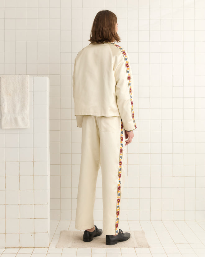 A person in a Candyfloss Jacket with a cream color, colorful side stripes, and an organza collar stands in a tiled room, facing away.