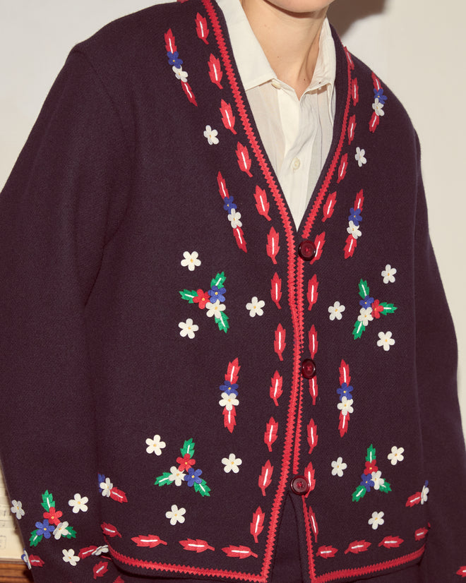 A person wears the Carroll Jacket—dark wool with colorful felted floral appliqué—over a white collared shirt, capturing a whimsical Alice through the Looking Glass vibe.