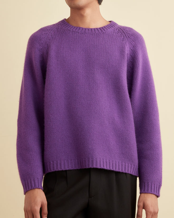 A person models the Cashmere Crewneck - Purple paired with black pants against a beige backdrop.