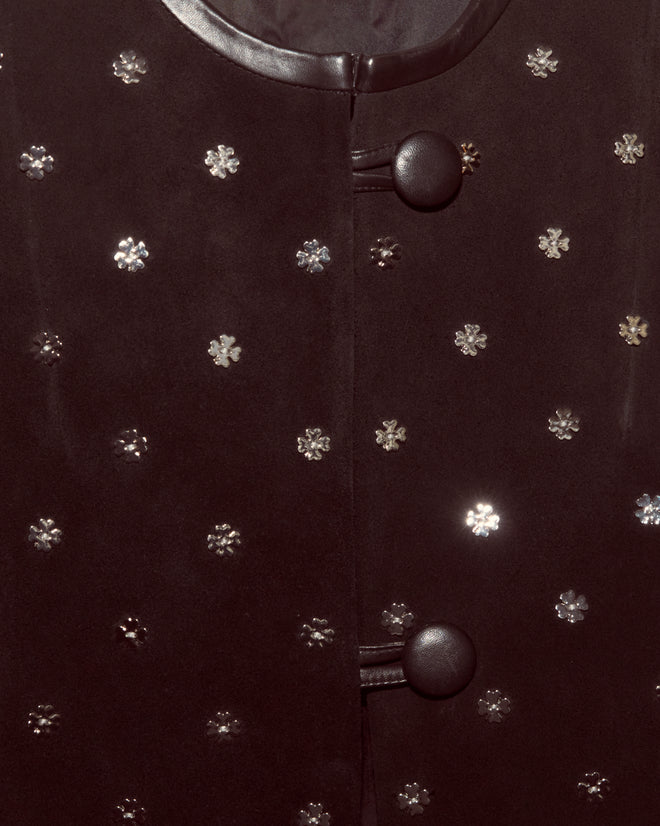Close-up of the Clover Charm Jacket, a black suede piece featuring two round buttons and small silver flower-shaped embellishments, showcasing its vintage-inspired charm and boxy silhouette.