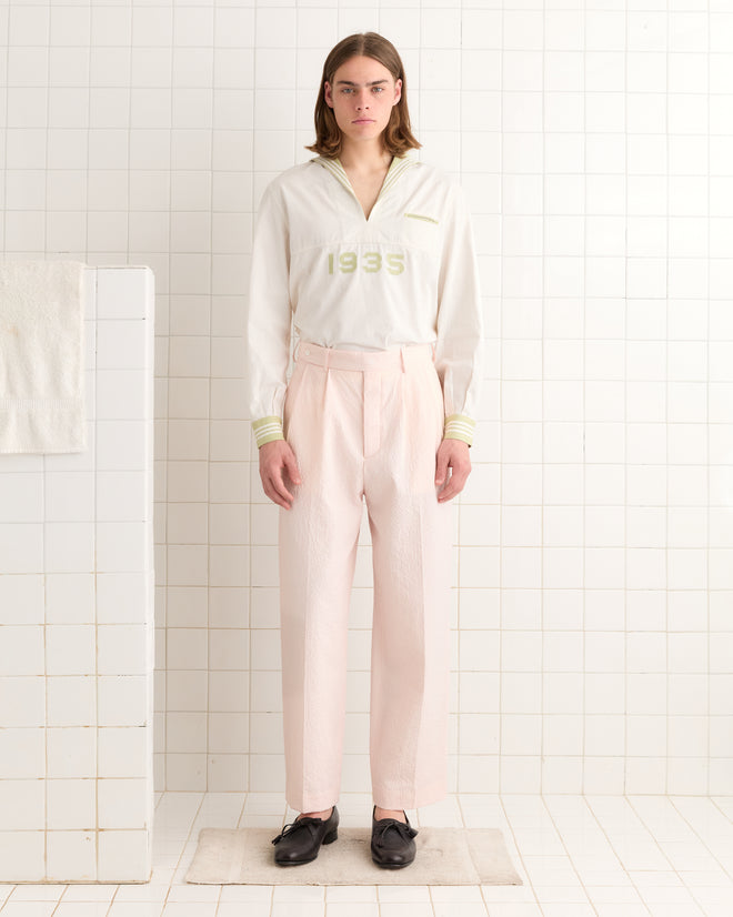A person in a white top and pink/white Club Stripe McNab Trousers stands on a mat in a tiled room.