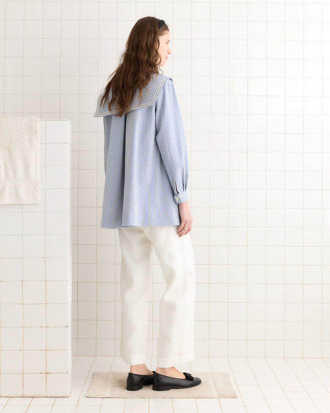 A woman stands on a mat in a tiled room, wearing the Club Stripe Sailor Coat in blue and white.