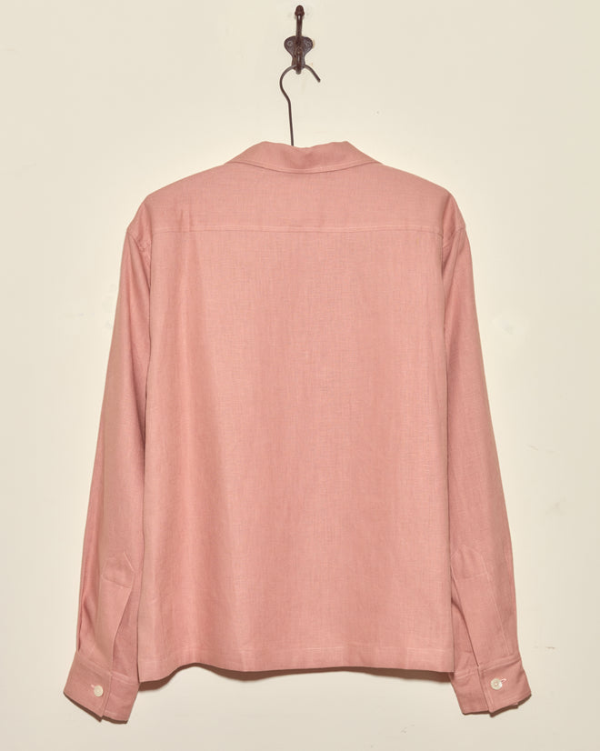 The Conch Shell Shirt - L, a unique pink long-sleeved top, is displayed from the back on a hook against a cream-colored wall.