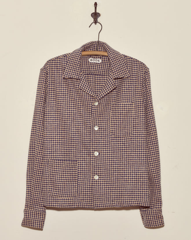 The Confetti Houndstooth Overshirt - S/M, a collared button-up made from deadstock wool, hangs on a wall hook.
