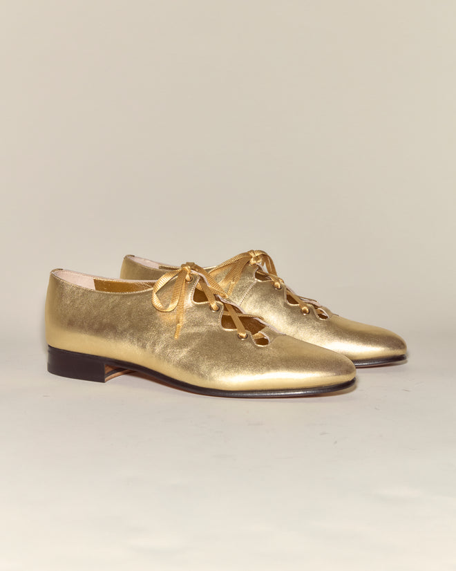 The County Clare Shoes - Metallic are shiny gold Italian leather lace-ups with low heels, made from metallic-treated leather and shown on a plain light background.