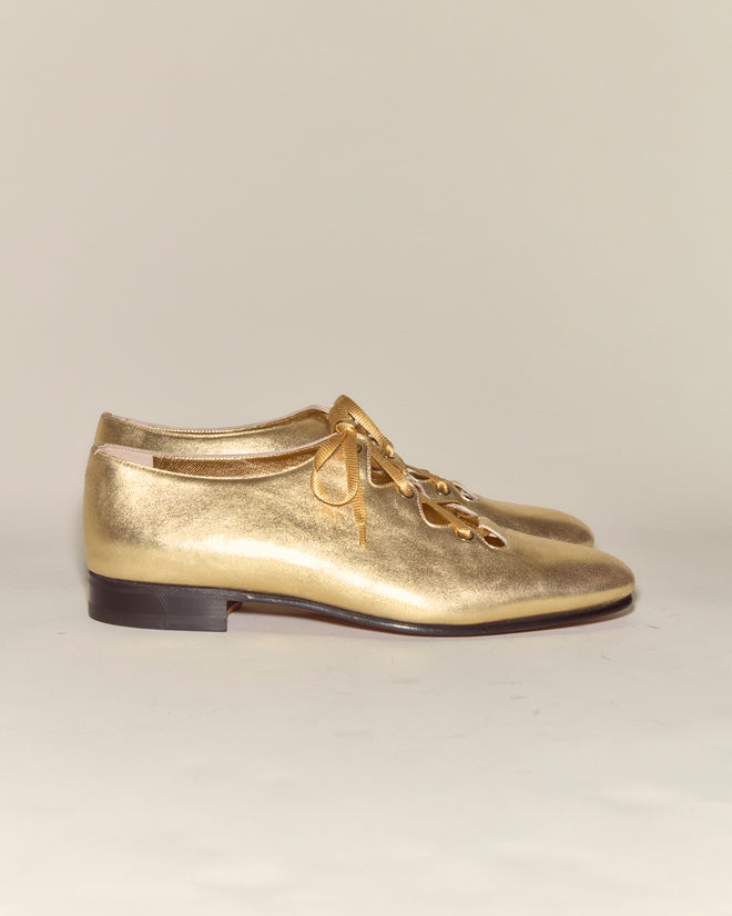 The County Clare Shoes - Metallic are shiny gold Italian leather shoes with a low heel, crafted from metallic-treated leather and shown on a light background.