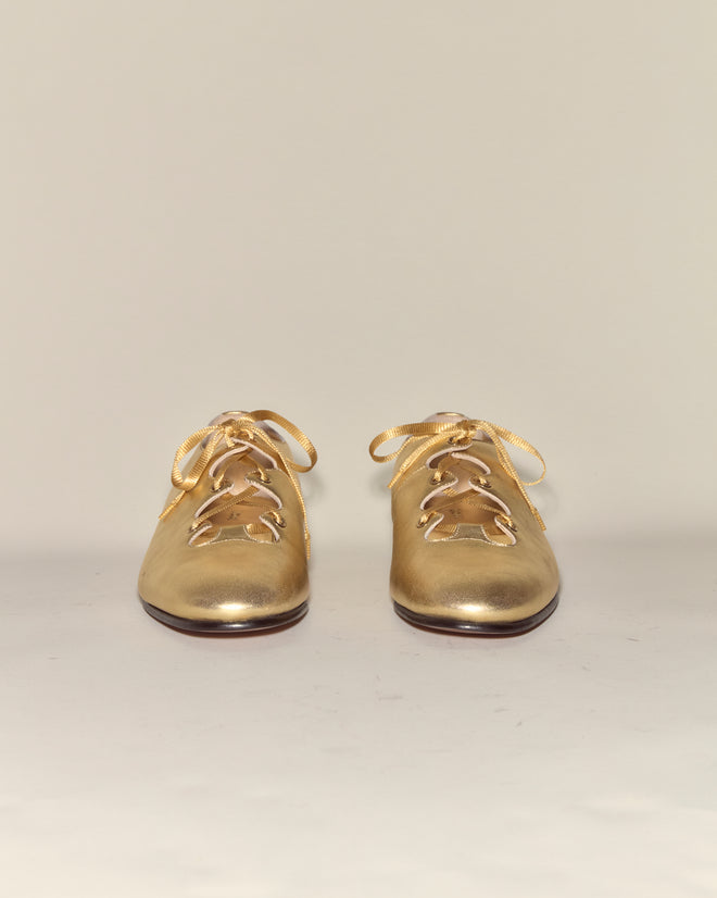 County Clare Shoes - Metallic: Italian leather baby shoes in shiny gold with bows and tree-shaped cutouts, crafted from metallic-treated leather, displayed on a plain light background.