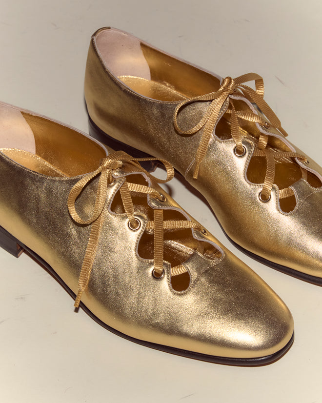 The County Clare Shoes - Metallic are shiny gold Italian leather shoes with ribbon laces, crafted from metallic-treated leather, and displayed on a light surface.