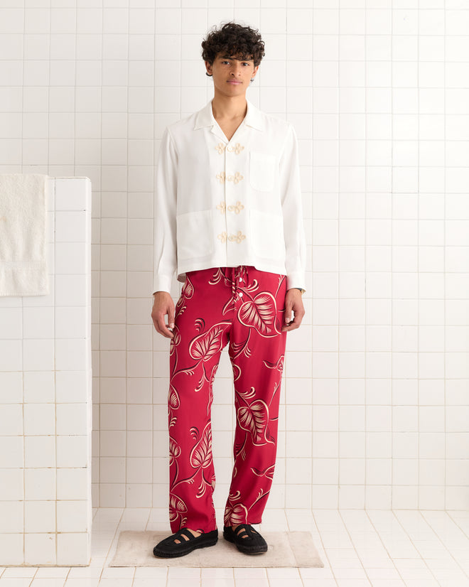 A person stands in a tiled room wearing a white shirt and Creeping Begonia Pajama Pants.