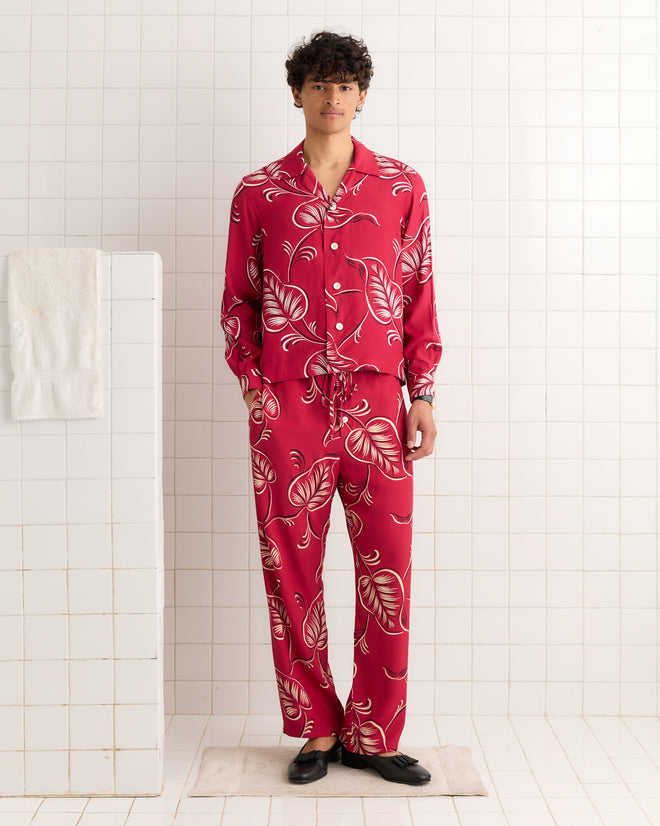 A man stands in a tiled bathroom wearing Creeping Begonia Pajama Pants and black slippers.