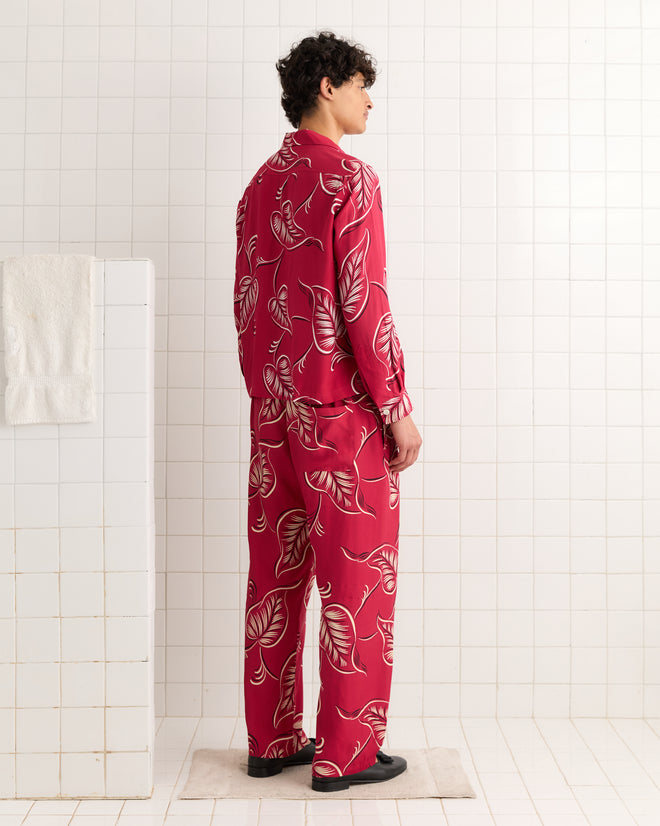 Someone wearing Creeping Begonia Pajama Pants with a red botanical print stands sideways in a white-tiled, midcentury-style bathroom.