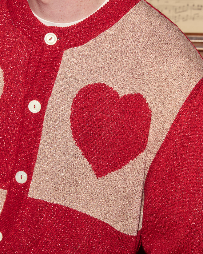 The Lamé Hearts Cardigan is a beige and red lightweight piece with a red heart pattern, white buttons, and shimmering lurex yarn accents.
