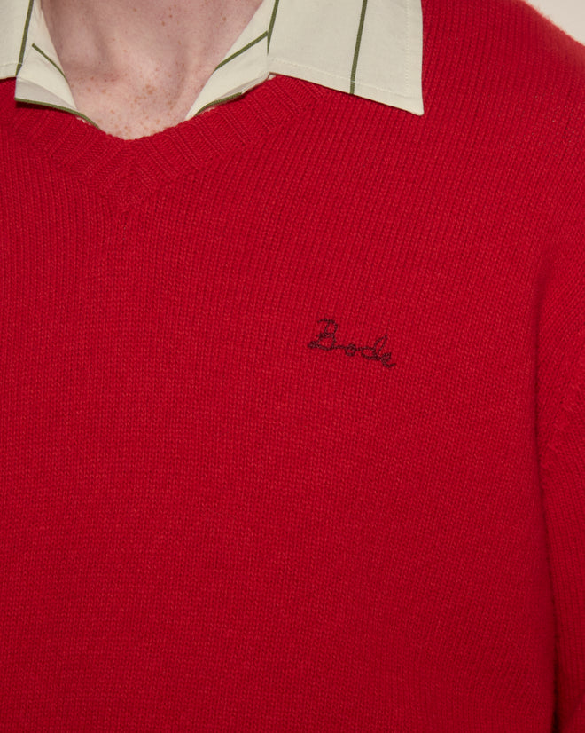 Close-up of a person wearing the Currant Sweater - Red, a wool cashmere blend V-neck, over a light green striped collared shirt.