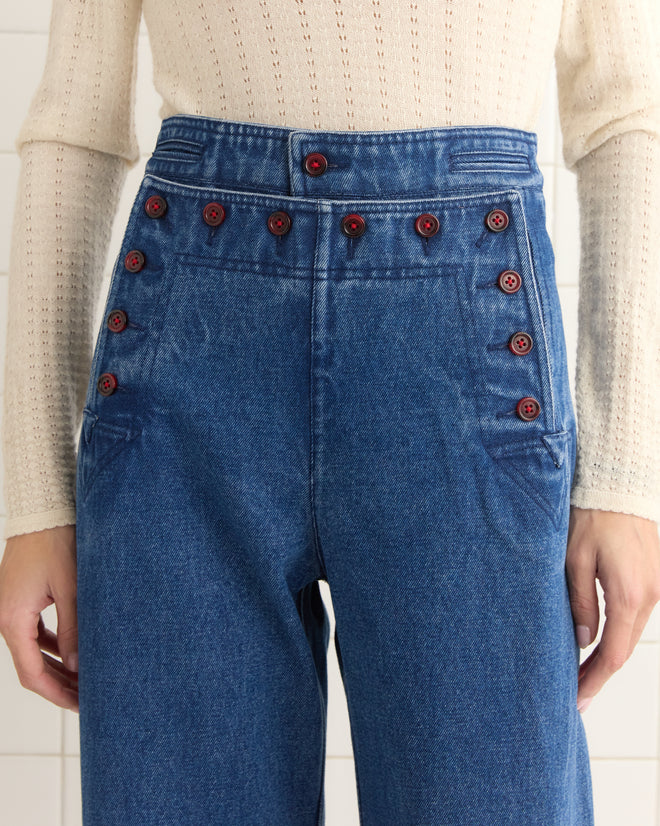 Someone in Denim Sailor Trousers, which are midweight, high-waisted navy pants with red buttons, paired with a cream sweater.