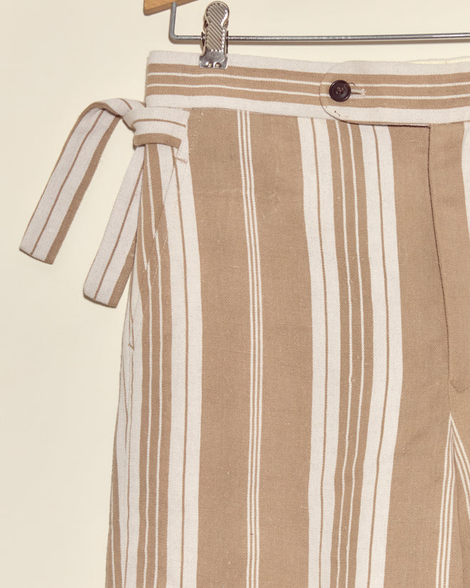 Desert Stripe Trousers: Beige and white striped deadstock twill pants with a side tie and button, displayed on a hanger.